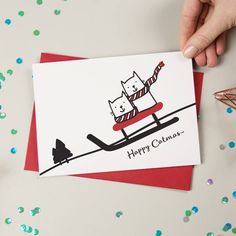 a hand holding a card with a cat on a sled