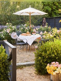 an outdoor dining area with table, chairs and umbrella in the middle of some bushes