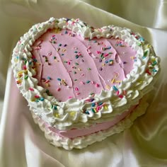 a pink heart shaped cake with sprinkles on it's edges and frosting