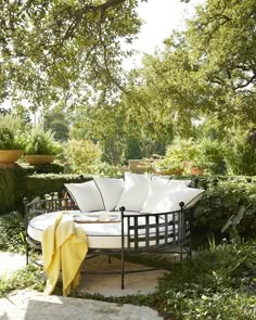 a white couch sitting on top of a lush green field next to a tree filled forest