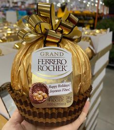 a hand holding a chocolate cupcake wrapped in gold foil with a bow on top