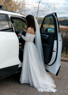 a woman in a wedding dress getting out of a white car with the door open