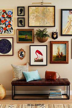 a wall filled with lots of framed pictures next to a wooden bench in front of a table