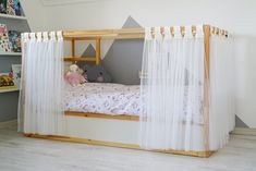 a child's bed with sheer curtains and a teddy bear on the bottom bunk