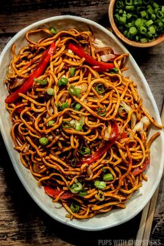 a plate full of noodles and vegetables with chopsticks next to it on a wooden table