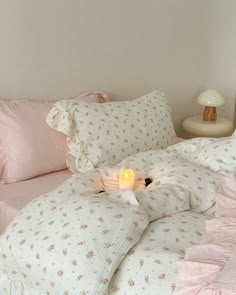 a bed with pink comforters and pillows on top of it next to a night stand