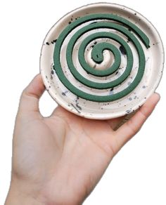 a hand holding a white bowl with green swirls on it's rim and bottom