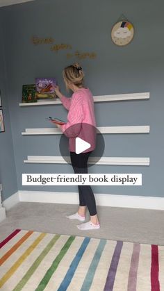 a woman standing in front of a book shelf on top of a colorful striped rug