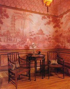 two chairs and a table in front of a wall with a painting on the wall