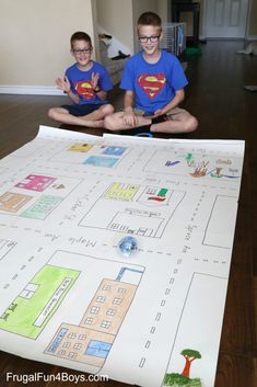 two young boys sitting on the floor in front of a large paper map with buildings