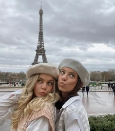 two beautiful young women standing next to each other in front of the eiffel tower