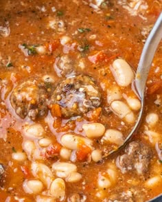 a ladle full of soup with meatballs and beans in it, ready to be eaten