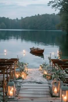 an outdoor ceremony setup with candles, flowers and a boat on the water at dusk