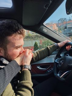 a man sitting in the driver's seat of a car with his hand on his mouth