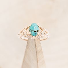 a turquoise stone ring sitting on top of a piece of wood in front of a white background