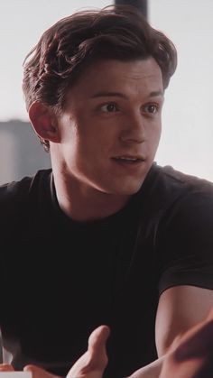 a young man sitting at a table with his hand up to the camera and looking off into the distance