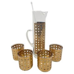 a pitcher and four glasses sitting next to each other on a white tablecloth with gold trimmings