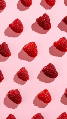 raspberries arranged in the shape of heart shapes on a pink background with shadows