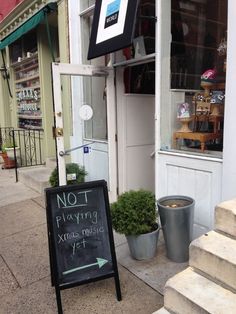 a sign that says not playing extra music yet in front of a store with potted plants