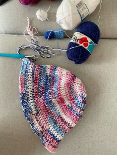 the crocheted hat is laying on the couch next to knitting needles and balls of yarn