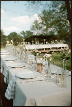 a long table with plates and vases filled with white flowers on top of it