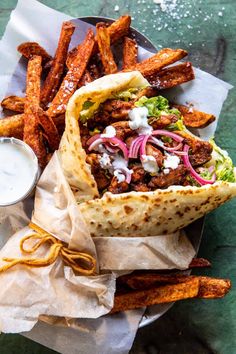 a pita filled with meat, onions and lettuce next to some fries