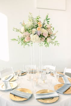 a white table with silver and gold place settings, flowers in tall vase on top