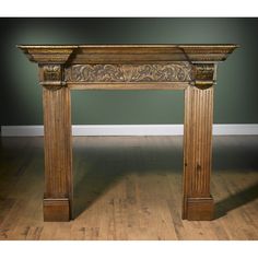 an antique style fireplace mantel with carvings on the top and sides, against a green wall