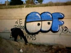 a man is painting graffiti on the side of a wall with blue and white letters