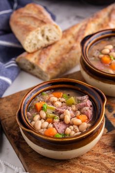 two bowls filled with soup sitting on top of a wooden cutting board next to bread