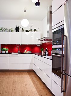 a modern kitchen with white cabinets and red backsplashing on the countertops