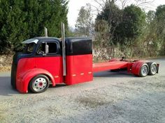 a red and black semi truck parked on the side of a road with trees in the background