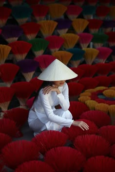 a woman sitting on the ground surrounded by red and yellow fan shaped umbrella's