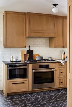 a kitchen with wooden cabinets and black tile flooring on the walls, along with a stainless steel stove top oven