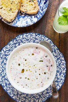 there is a bowl of soup next to two plates with bread and drinks on the table