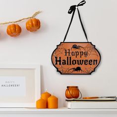 a happy halloween sign hangs on the wall next to candles and pumpkins in front of a white fireplace