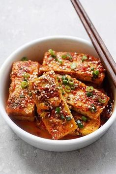 a bowl filled with tofu and chopsticks on top of a white table