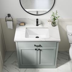 a white sink sitting under a round mirror in a bathroom next to a wall mounted toilet