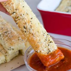 a person dipping something into a small bowl of sauce with bread sticks sticking out of it