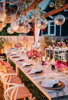 a long table set up for a party with pink flowers and disco balls hanging from the ceiling