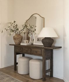 a wooden table with two stools and a lamp on top of it next to a mirror