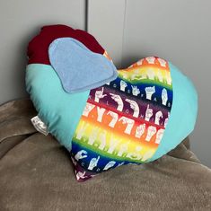 a colorful heart shaped pillow sitting on top of a brown couch next to a wall