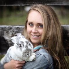 a woman holding a small rabbit in her arms and smiling at the camera while sitting on a bench