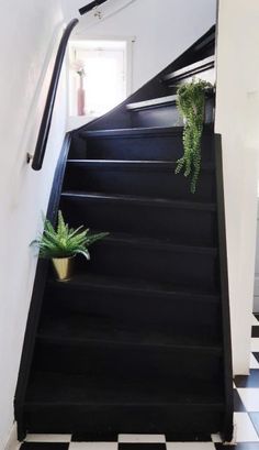 a black and white tiled floor next to a stair case with a plant on it