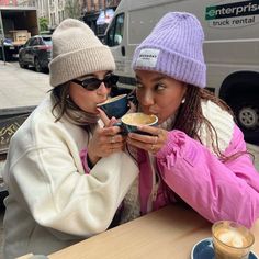 two women sitting at a table eating food and drinking from cups in front of them