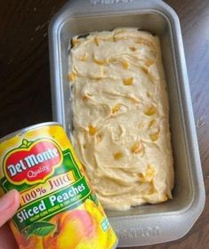 a person holding a can of peach ice cream next to a container of sliced peaches