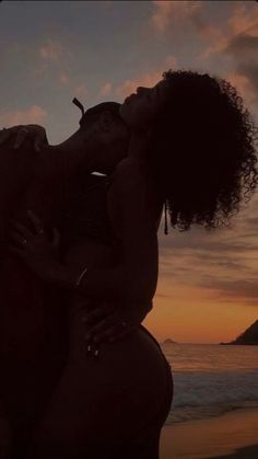 a woman kissing another woman on the beach at sunset, with an ocean in the background