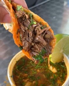 a hand holding a tortilla filled with meat and vegetables over a bowl of soup