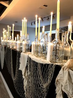 many wine bottles are lined up on a long table with candles and cloths wrapped around them