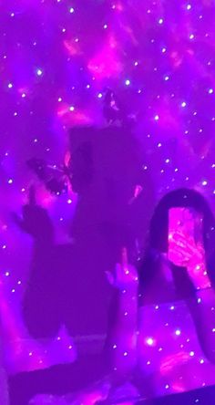 two people standing in front of a purple light with their cell phones up to their ears